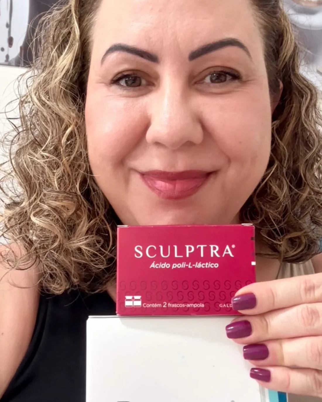 Dra. Adriana Bernardes sorrindo e segurando as caixas dos bioestimuladores Sculptra e Radiesse
