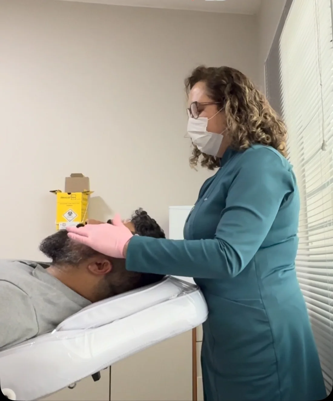 Dra. Adriana, de luvas e máscara, examinando o rosto de um paciente deitado na maca